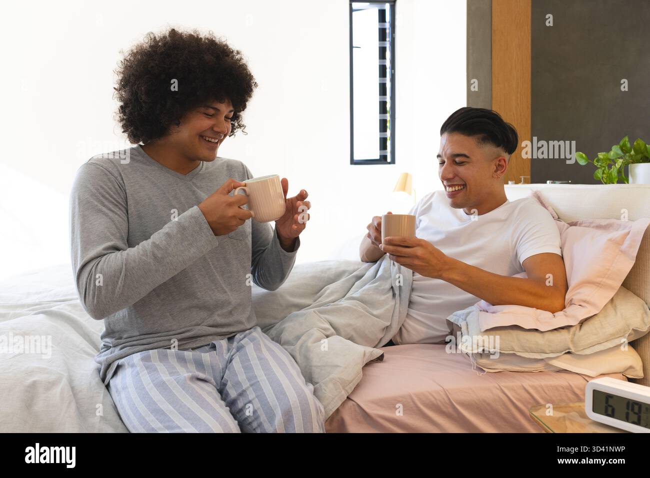 Relaxer divers amis masculins sirotant des tasses en céramique sur le lit dans une chambre moderne et lumineuse Banque D'Images