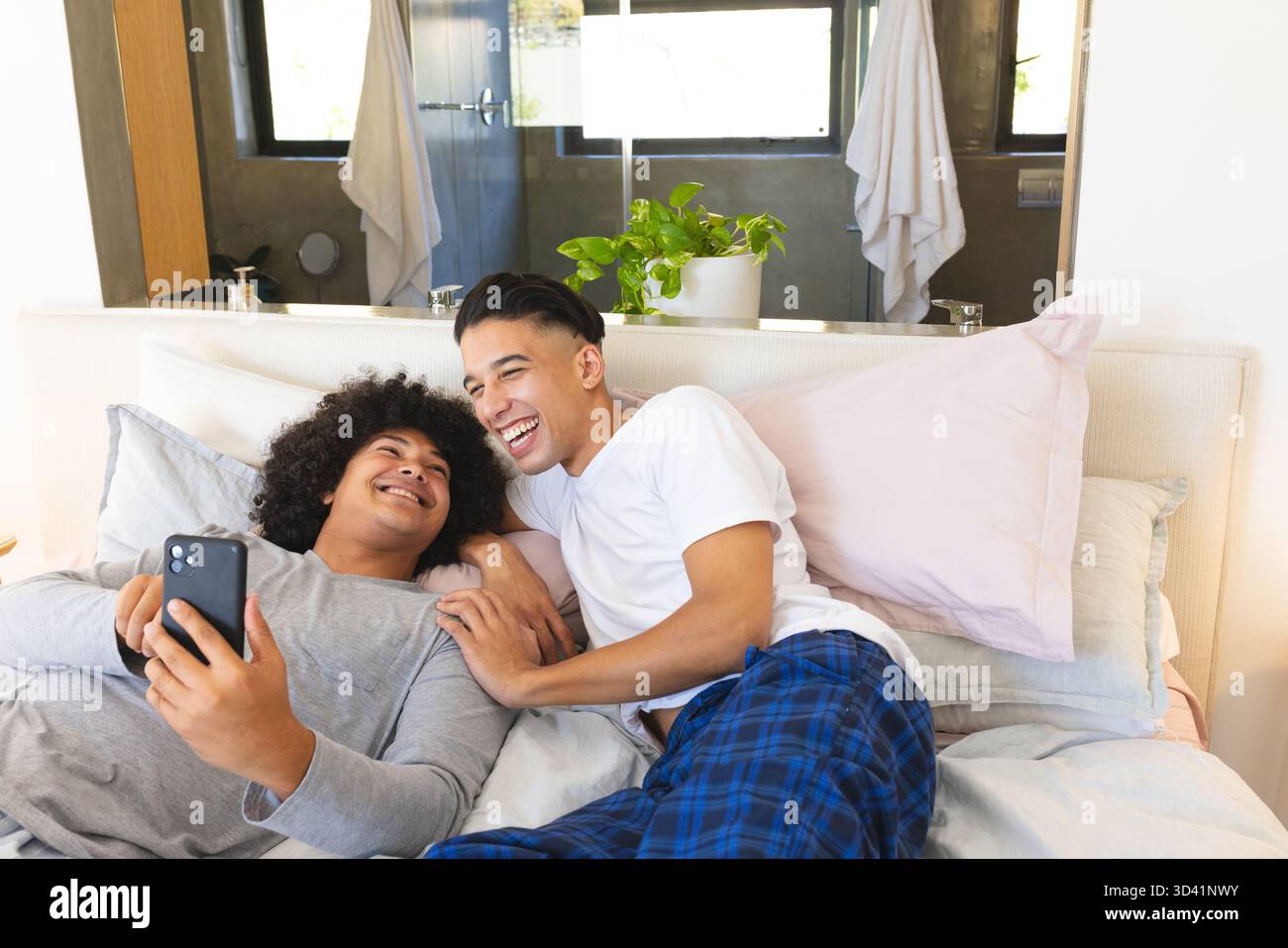 Rire divers amis masculins prenant selfie dans une chambre confortable, avec des oreillers pastel et smartphone Banque D'Images
