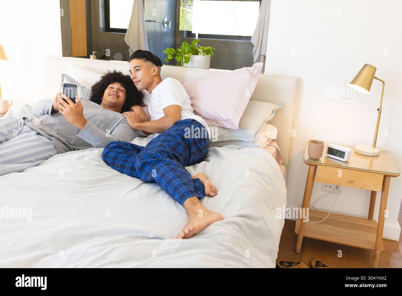 Se prélasser divers hommes partageant smartphone sur le lit dans une chambre moderne, avec tasse à café et pantoufles Banque D'Images