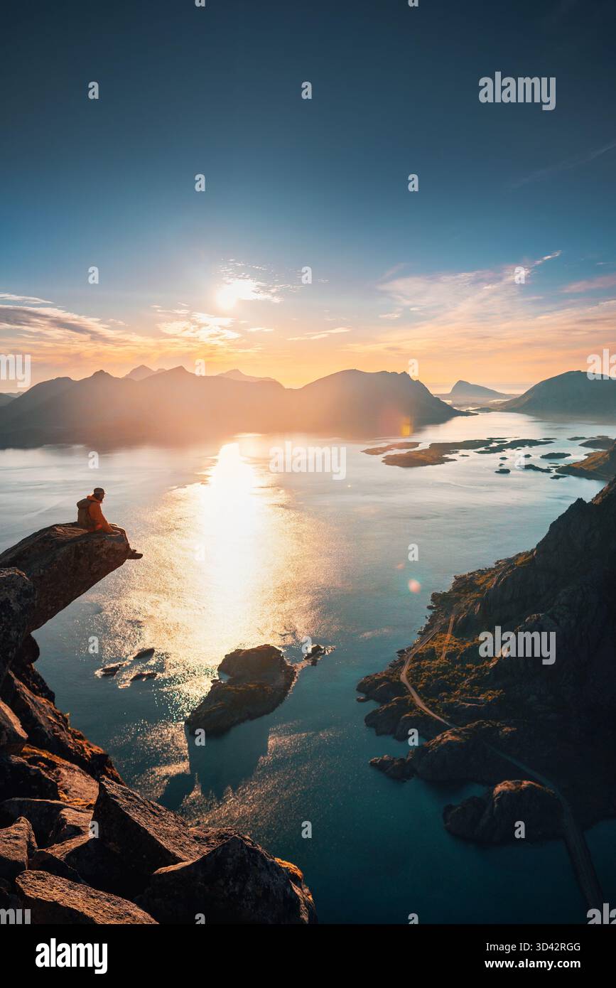 Voyage épique dans les îles Lofoten - homme assis sur le bord de la falaise de Torsketunga au-dessus des montagnes d'escalade de mer en solo en Norvège, excursion d'aventure extrême active summ Banque D'Images