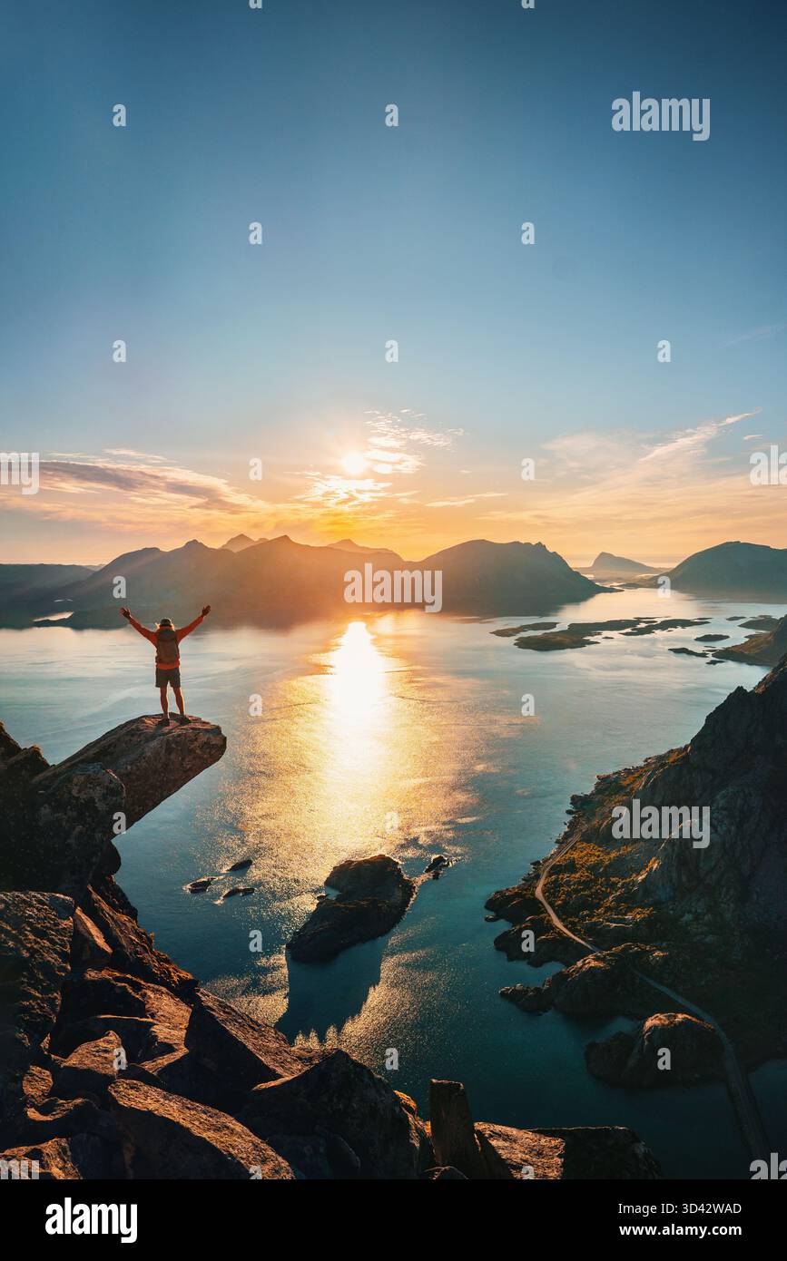 Homme voyageant seul en Norvège grimpant au bord de la falaise Torsketunga dans les îles Lofoten, voyageur courageux appréciant les montagnes et la mer vue aérienne aventure vacat Banque D'Images