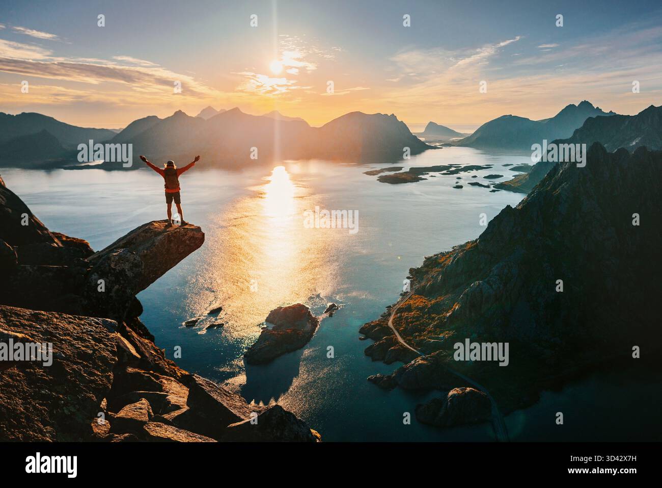 Homme grimpeur voyage en Norvège debout sur le bord de la falaise Torsketunga dans les îles Lofoten profitant des montagnes de coucher du soleil et vue sur la mer, voyage d'aventure extrême en t Banque D'Images
