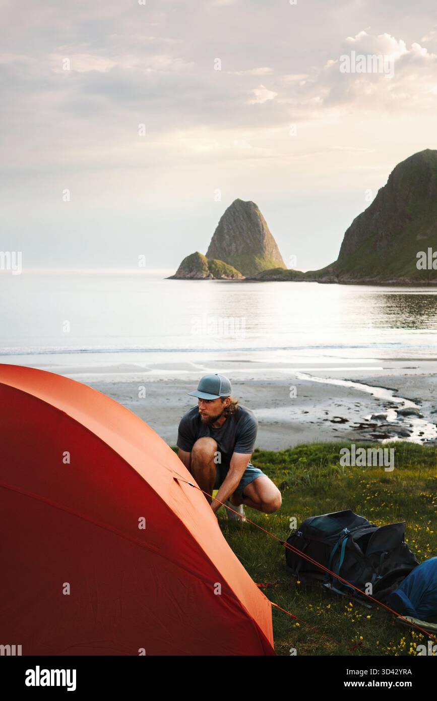 Homme voyageant en solo mettant en place le matériel de camping de tente sur la plage en Norvège randonnée aventure en plein air, style de vie sain vacances actives d'été expedi Banque D'Images
