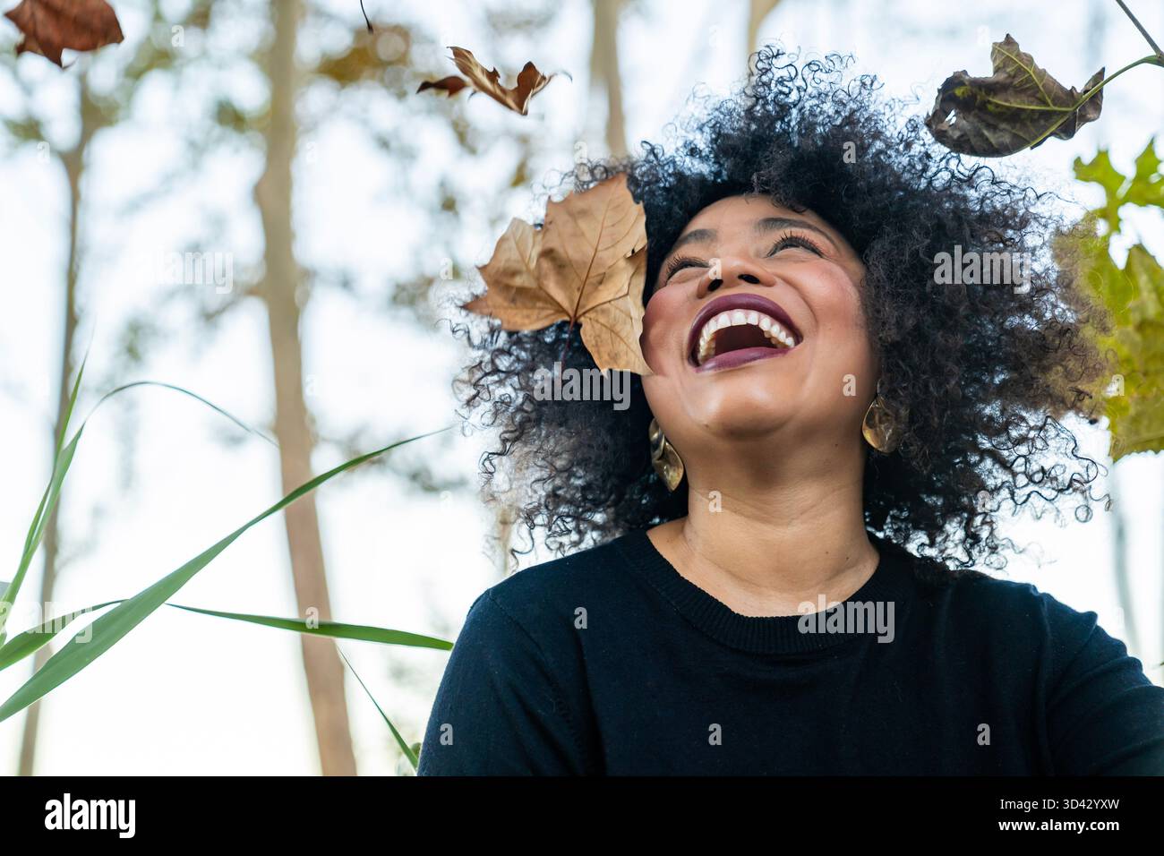 Heureuse jeune femme appréciant la chute des feuilles d'automne dans un cadre extérieur, exprimant la joie Banque D'Images