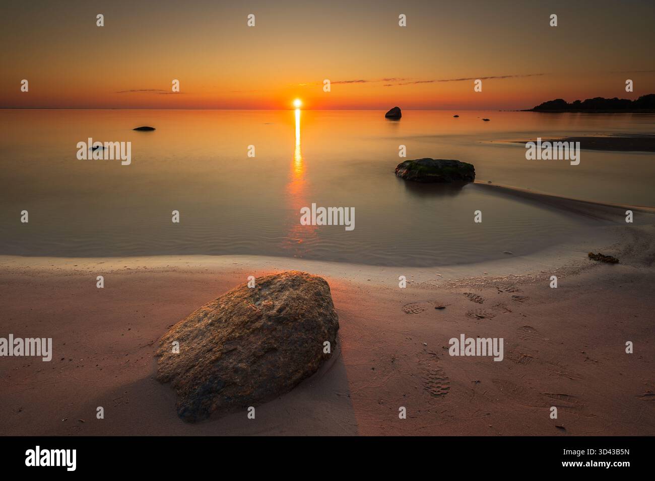 Paysage marin lisse du soir avec un grand rocher sur la plage pendant le coucher de soleil coloré et la mer calme. Lahemaa, Estonie. Banque D'Images