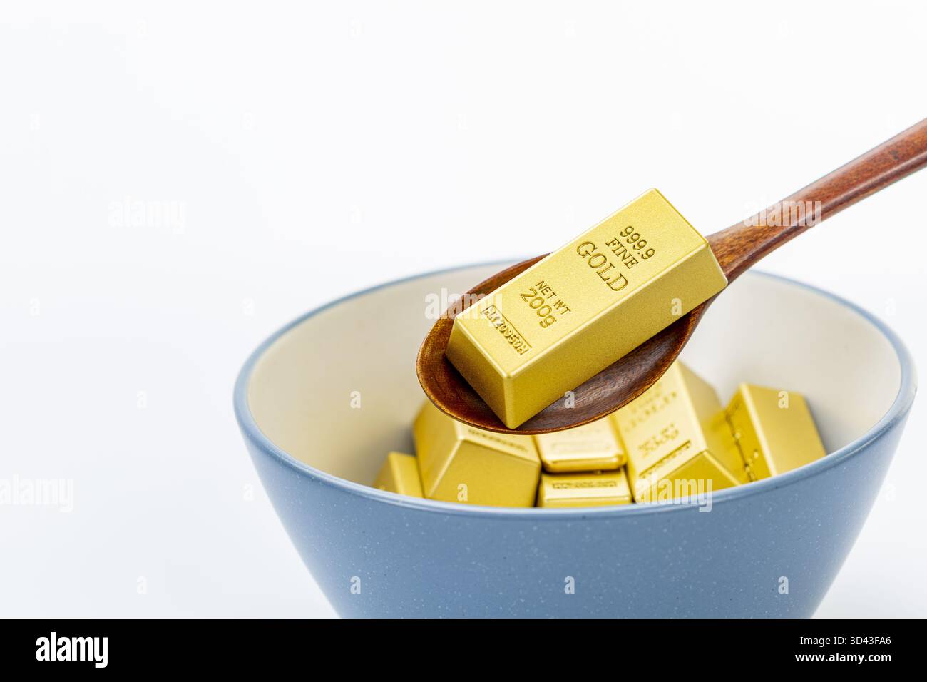 Délicatement creuser des lingots d'or avec une cuillère dans un bol en céramique bleu et blanc sur un fond blanc propre, symbolisant la richesse, le luxe, la prospérité Banque D'Images