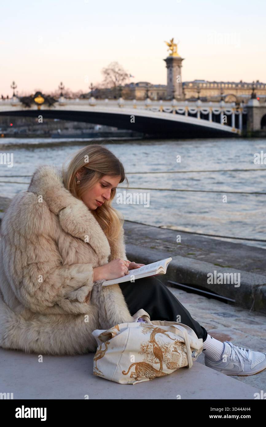 Femme écrivant au bord de la Seine à Paris pendant le coucher du soleil sur une soirée fraîche, Paris, France Banque D'Images
