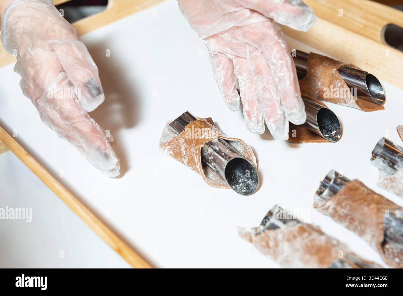 Nourriture, les mains gantées façonnent soigneusement la pâte à pâtisserie au chocolat autour de moules métalliques sur un plateau pour la préparation de cuisson dans un cadre de cuisine Banque D'Images