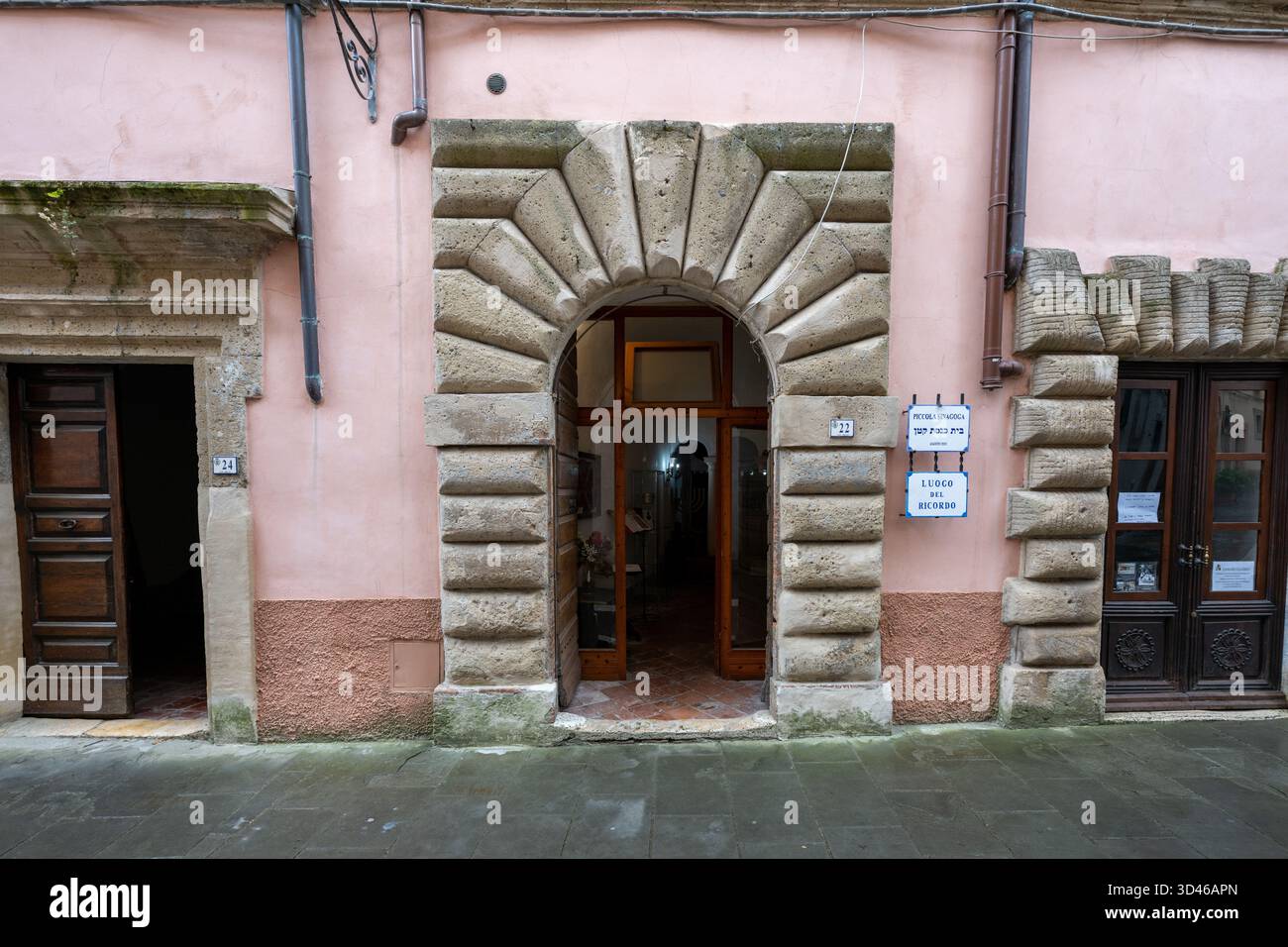 Entrée de la petite synagogue de Sorano, Italie, avec une arche en pierre rustique et une façade pastel. Le bâtiment présente une architecture traditionnelle Banque D'Images