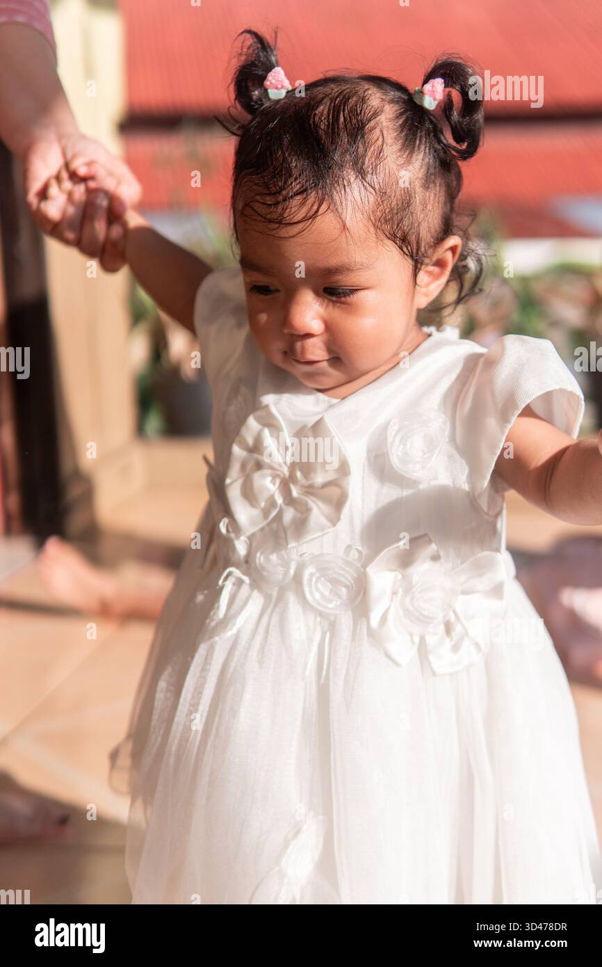 Un portrait franc d'une jolie petite fille asiatique dans une robe blanche, assise avec sa mère. Les deux regardent loin réfléchi sur un porche ensoleillé dans une maison chaude. Banque D'Images