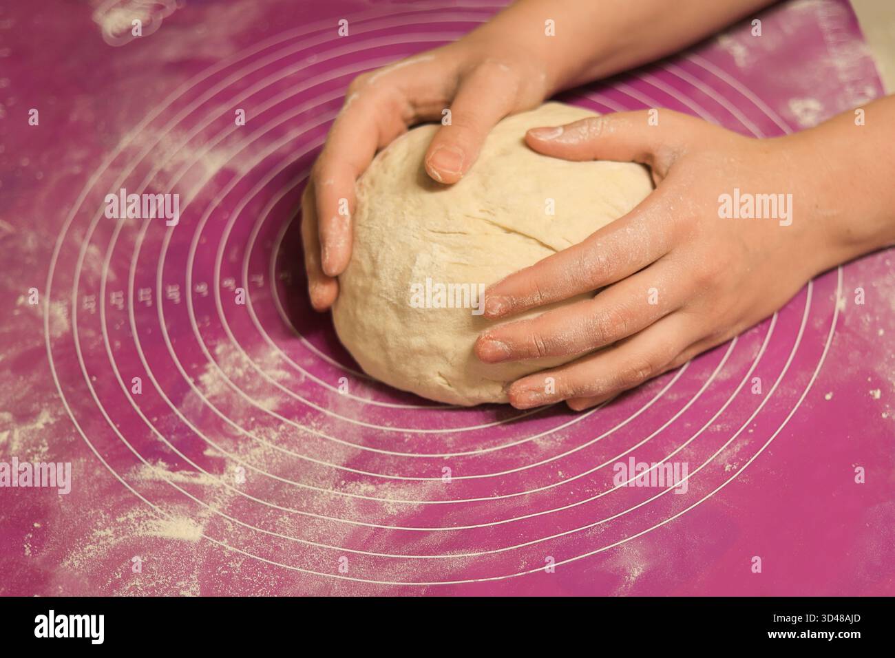 Un gros plan des mains façonnant et arrondissant doucement une grande boule de pâte fraîche sur un tapis de cuisson en silicone rose saupoudré de farine. Photo de haute qualité Banque D'Images