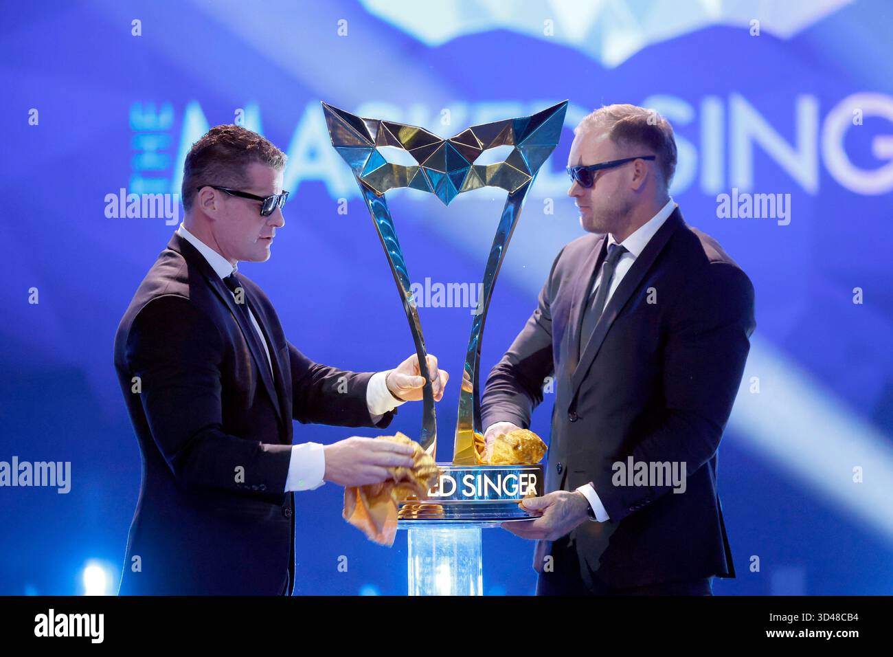Der Pokal für den Sieger von The Masked Singer mit dem logo der Show wird von zwei Security-Mitarbeitern in der ProSieben-Show the Masked Singer in den MMC-Studios in Ossendorf poliert. Themenbild, Symbolbild Köln, 08.11.2025 NRW Deutschland *** le trophée pour le vainqueur du chanteur masqué avec le logo des spectacles est poli par deux agents de sécurité dans le spectacle ProSieben le chanteur masqué aux studios MMC à Ossendorf image thématique, image symbolique Cologne, 08 11 2025 NRW Allemagne Copyright : xChristophxHardtx Banque D'Images