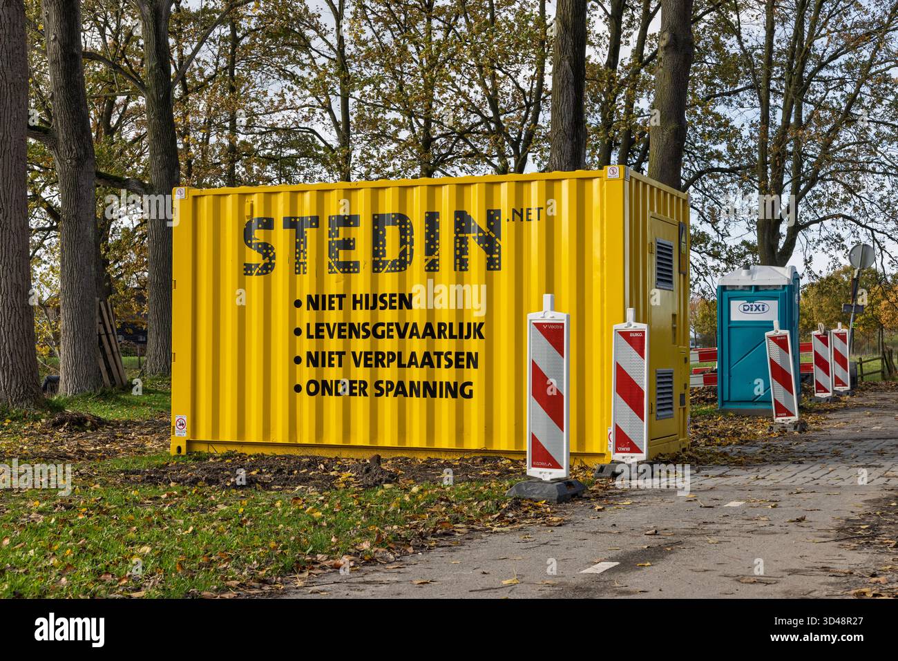 Conteneur Stedin jaune avec avertissements de danger en néerlandais (« danger pour la vie », « sous-tension ») placé dans une zone boisée pendant les travaux de construction. Banque D'Images