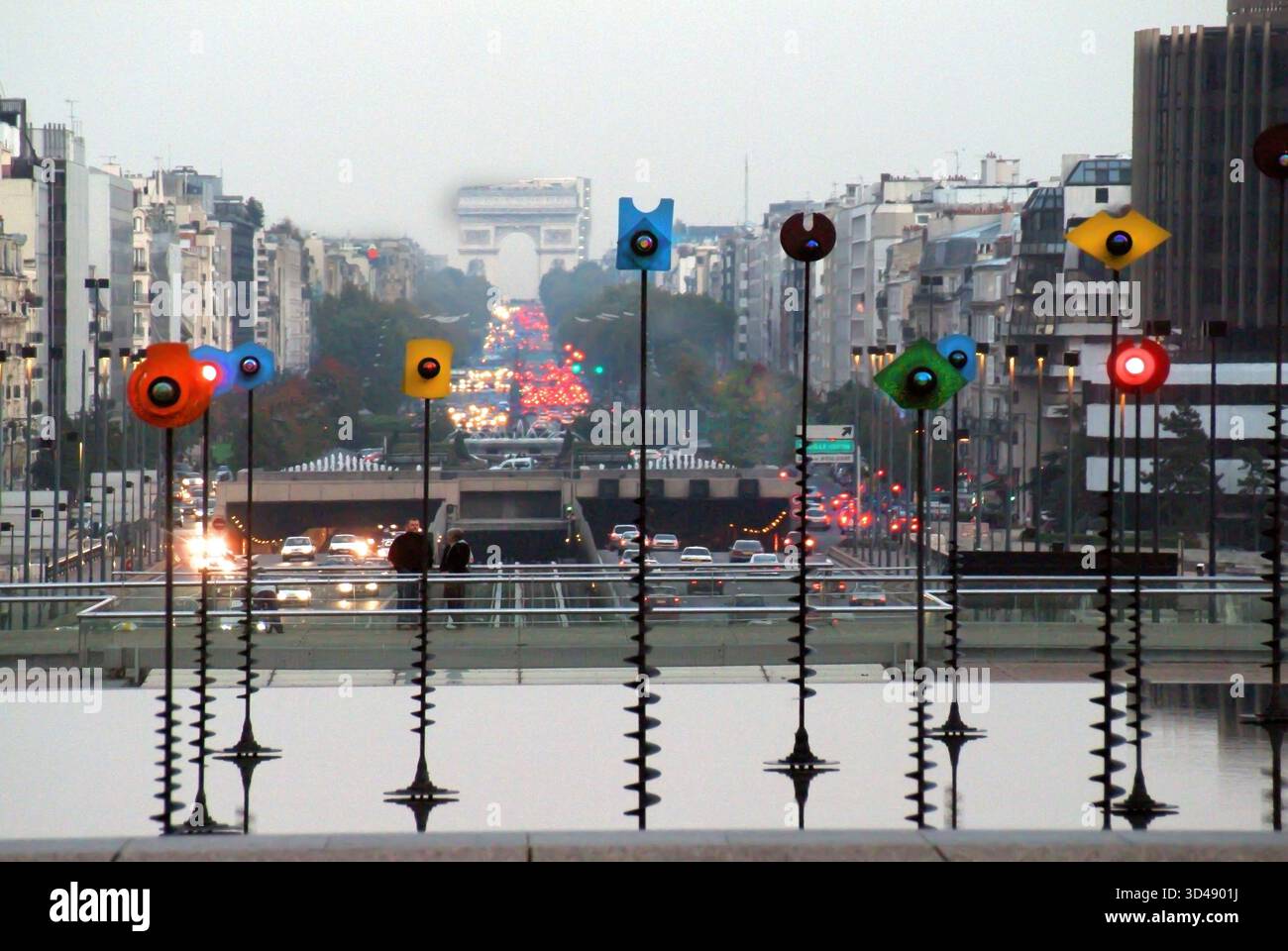 Image d'archive prise en l'an 2003 du paysage urbain de Paris vu au-delà du premier plan d'une petite partie de l'œuvre connue sous le nom de bassin Takis une piscine d'eau carrée plate de 50 mètres dans le parc d'affaires de la Défense une installation conçue par l'artiste grec Panayiotis Vassilakis également connu sous le nom de Takis. Certains des 49 feux clignotants colorés de forme géométrique sont montrés ici répartis sur une petite partie de l'eau de la piscine avec des spectateurs sur la plate-forme d'observation regardant la circulation nocturne sur les champs-Élysées vers l'Arc de Triomphe lointain (Arc de Triomphe) dans un ciel brumeux en France UE Banque D'Images