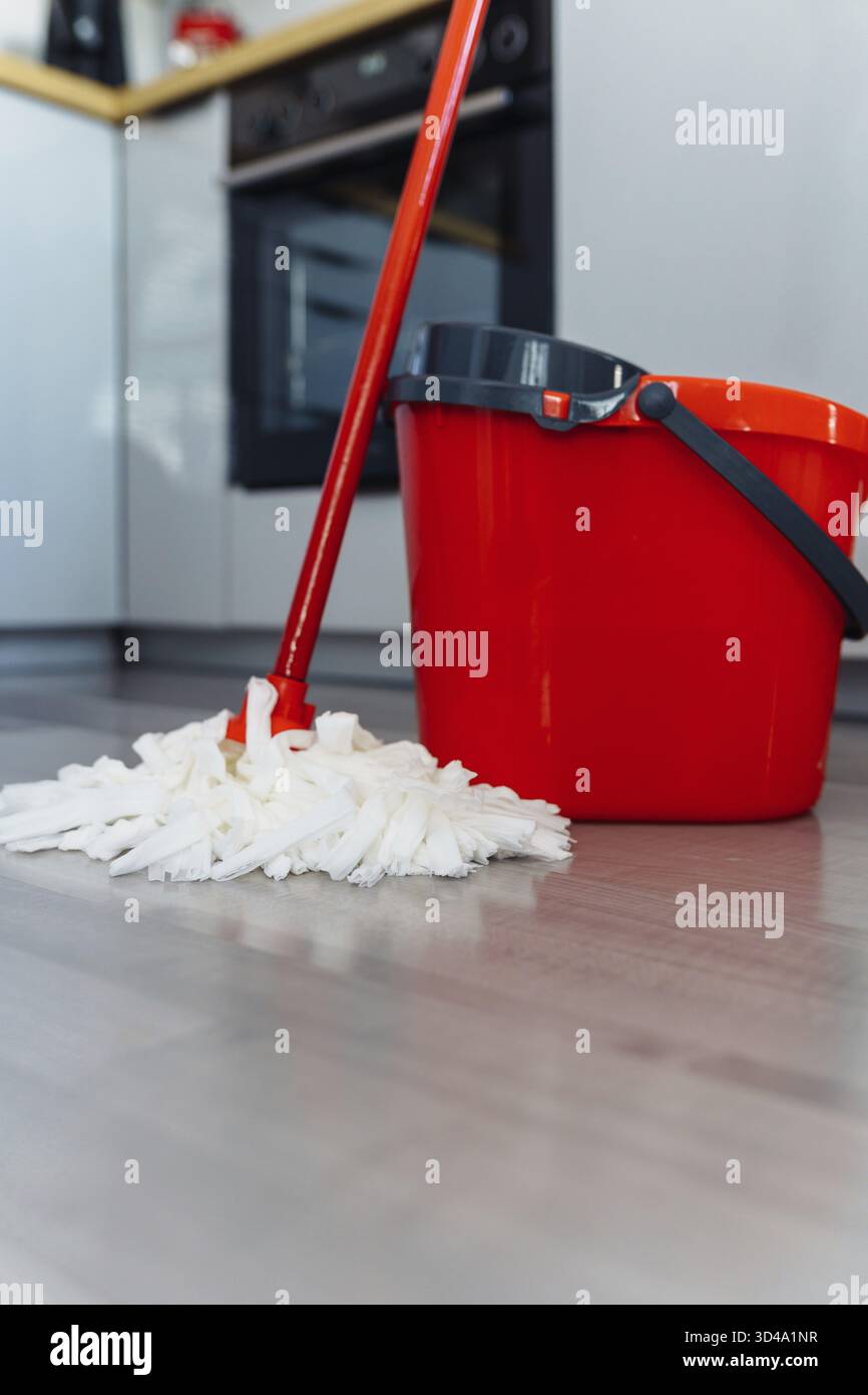Seau de nettoyage humide rouge avec essoreuse à eau et balai à franges sur le sol avec revêtement gris Banque D'Images