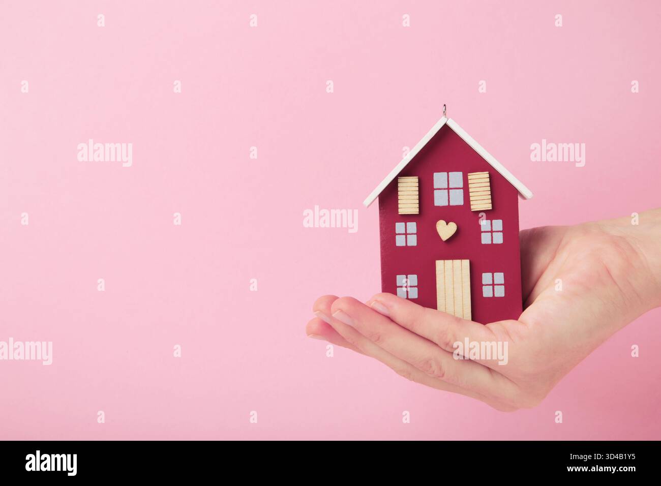 Mains avec maison de jouet en bois sur fond rose. Vue de dessus Banque D'Images