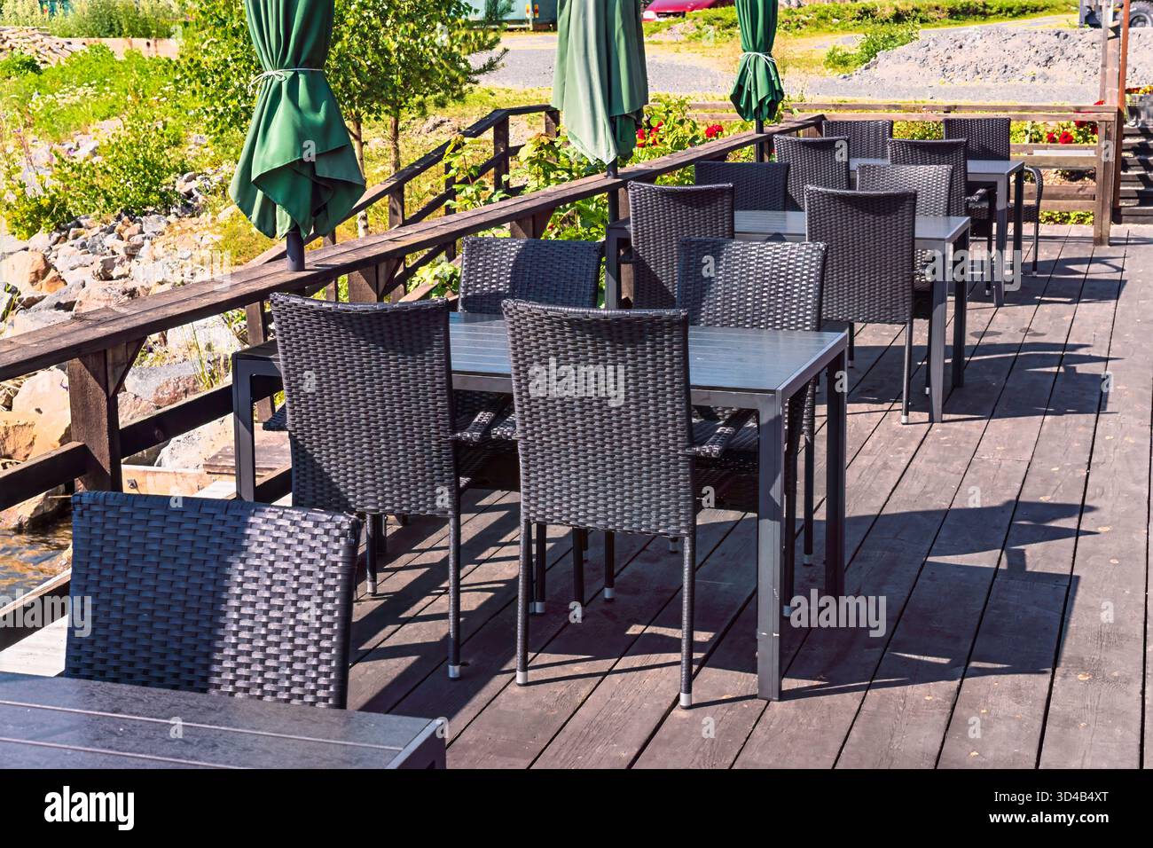 Terrasse de restaurant vide en plein air par une journée ensoleillée à Axmar, en Suède, avec des rangées de chaises en osier sombre, des tables et des parasols pliés verts, invitant RELA Banque D'Images