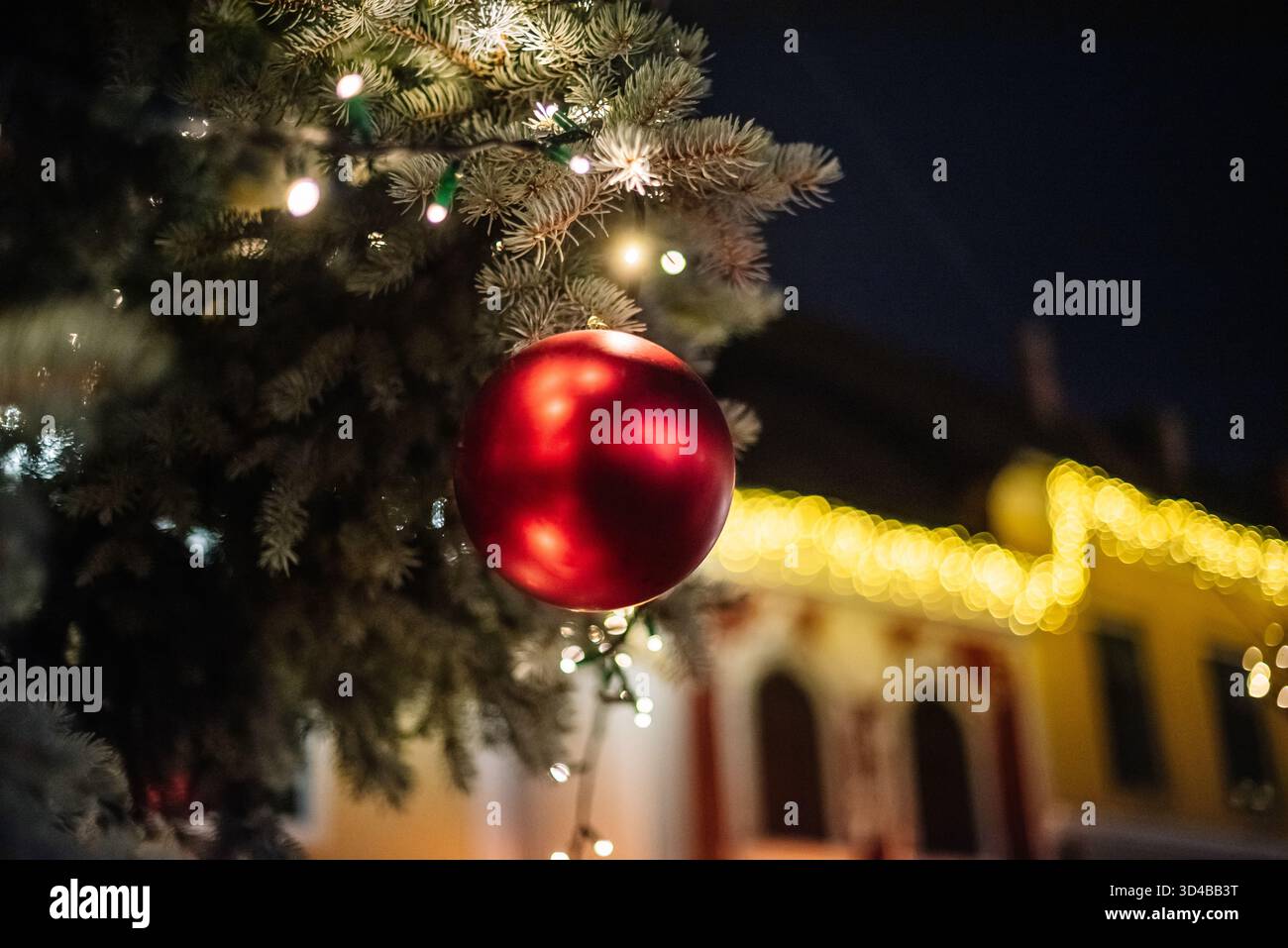 Ornement de Noël rouge sur un sapin avec des lumières festives la nuit Banque D'Images