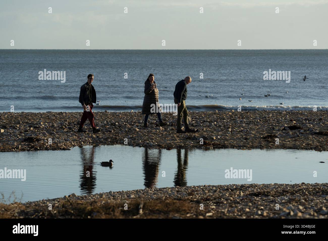 Les gens marchent sur une plage de galets près de la mer à Charmouth, Dorset Banque D'Images
