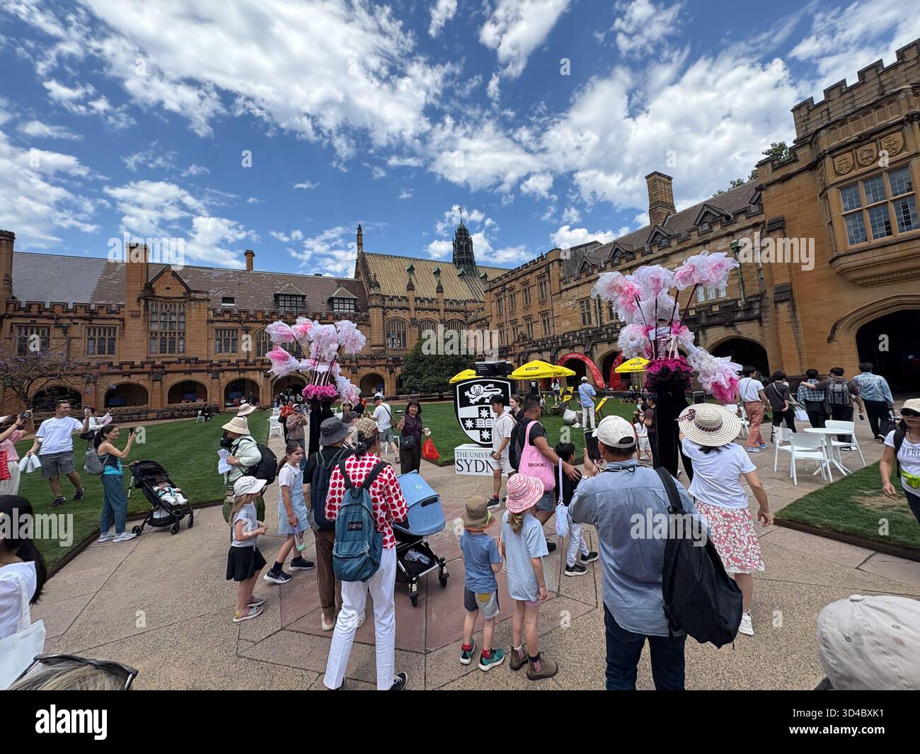 Le quadriangle de l'Université de Sydney est animé par des personnes assistant à un événement, avec une architecture gothique historique, des artistes et un ciel bleu clair en S. Banque D'Images