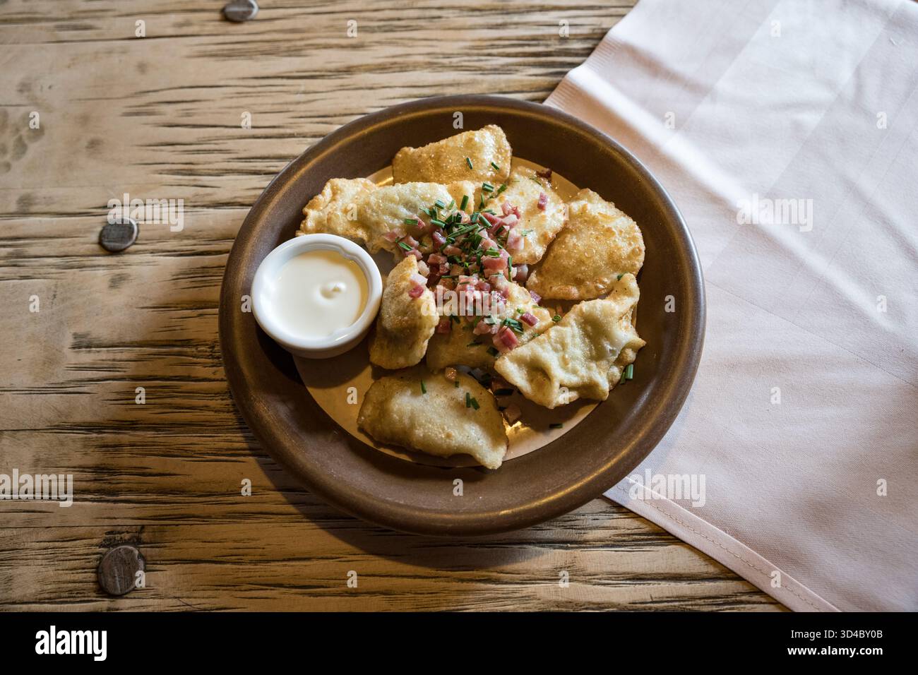 Piérogies polonaises classiques avec garniture de jambon et d'échalotes servies sur une assiette brune en terre au-dessus d'une serviette en lin et d'une table en bois. Banque D'Images