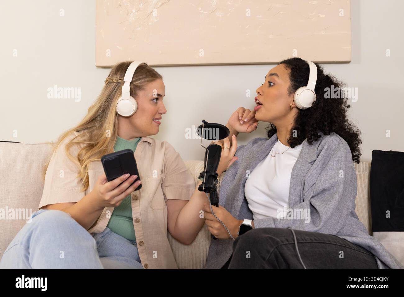 Enregistrement de diverses hôtes féminines discutant dans le home studio, avec écouteurs, smartphone et microphone Banque D'Images