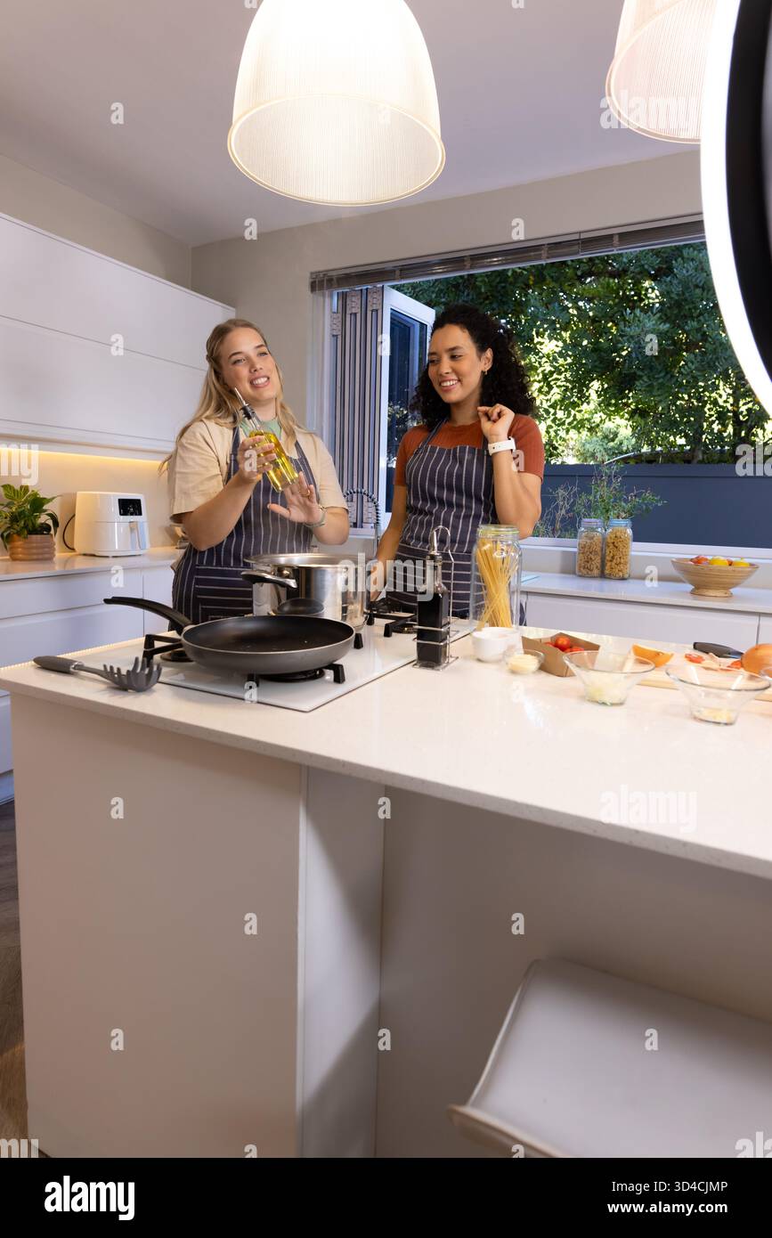 Cuisiner diverses amies préparant des pâtes à l'îlot de cuisine, avec de l'huile d'olive et un pot à spaghetti Banque D'Images
