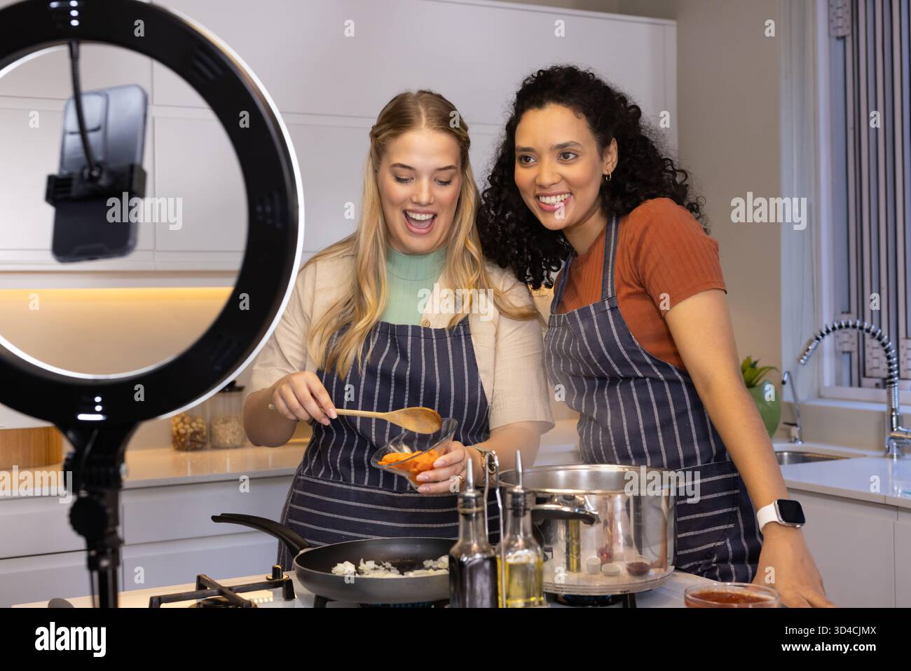 Filmer diverses amies cuisinant sur un îlot de cuisine lumineux, avec éclairage annulaire et support de téléphone Banque D'Images