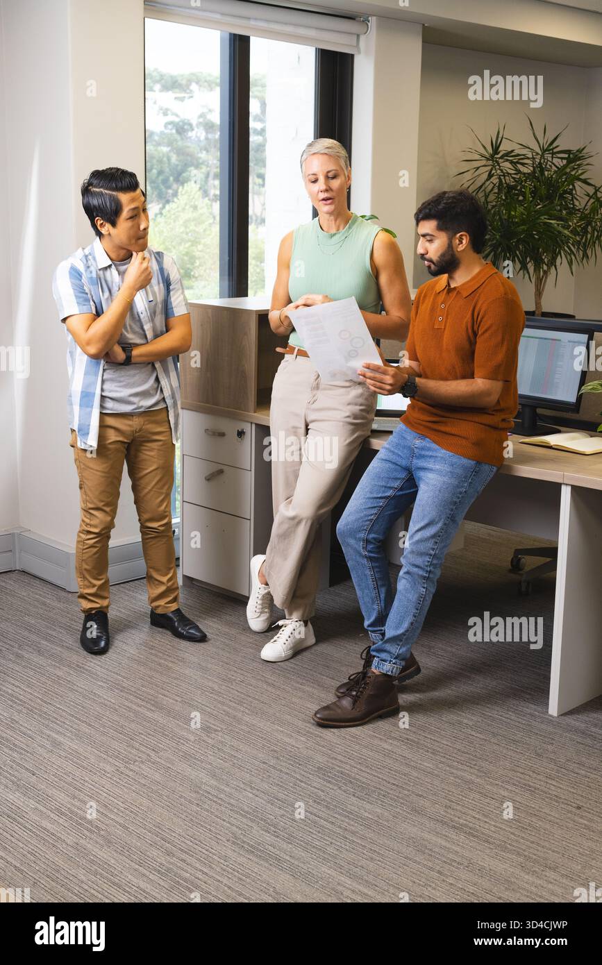Divers collègues examinant les diagrammes imprimés au bureau, avec moniteur et usine Banque D'Images