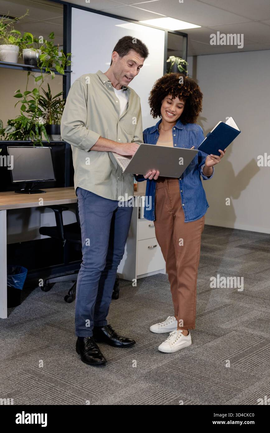 Analyse du rapport divers collègues collaborant dans un bureau ouvert, tenant un ordinateur portable et un ordinateur portable Banque D'Images