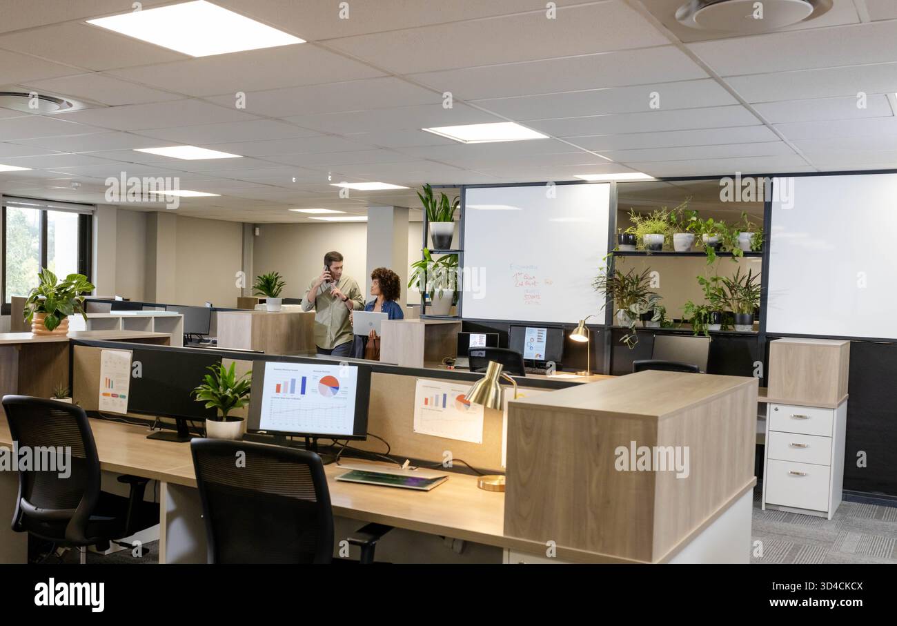Debout divers collègues discutant des cartes dans un bureau moderne ouvert, avec tablette et smartphone Banque D'Images