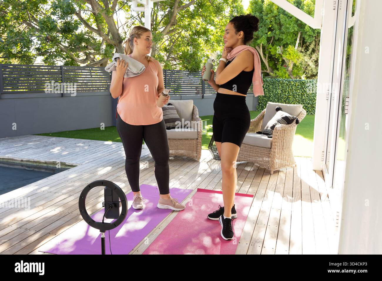 Bavardez diverses amies féminines sur le patio en bois à côté de la piscine, avec des tapis de yoga et un anneau lumineux Banque D'Images
