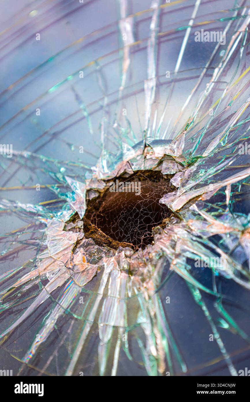 Gros plan d'un pare-brise brisé avec trou de balle, montrant des éclats brisés et des fissures radiales. Banque D'Images