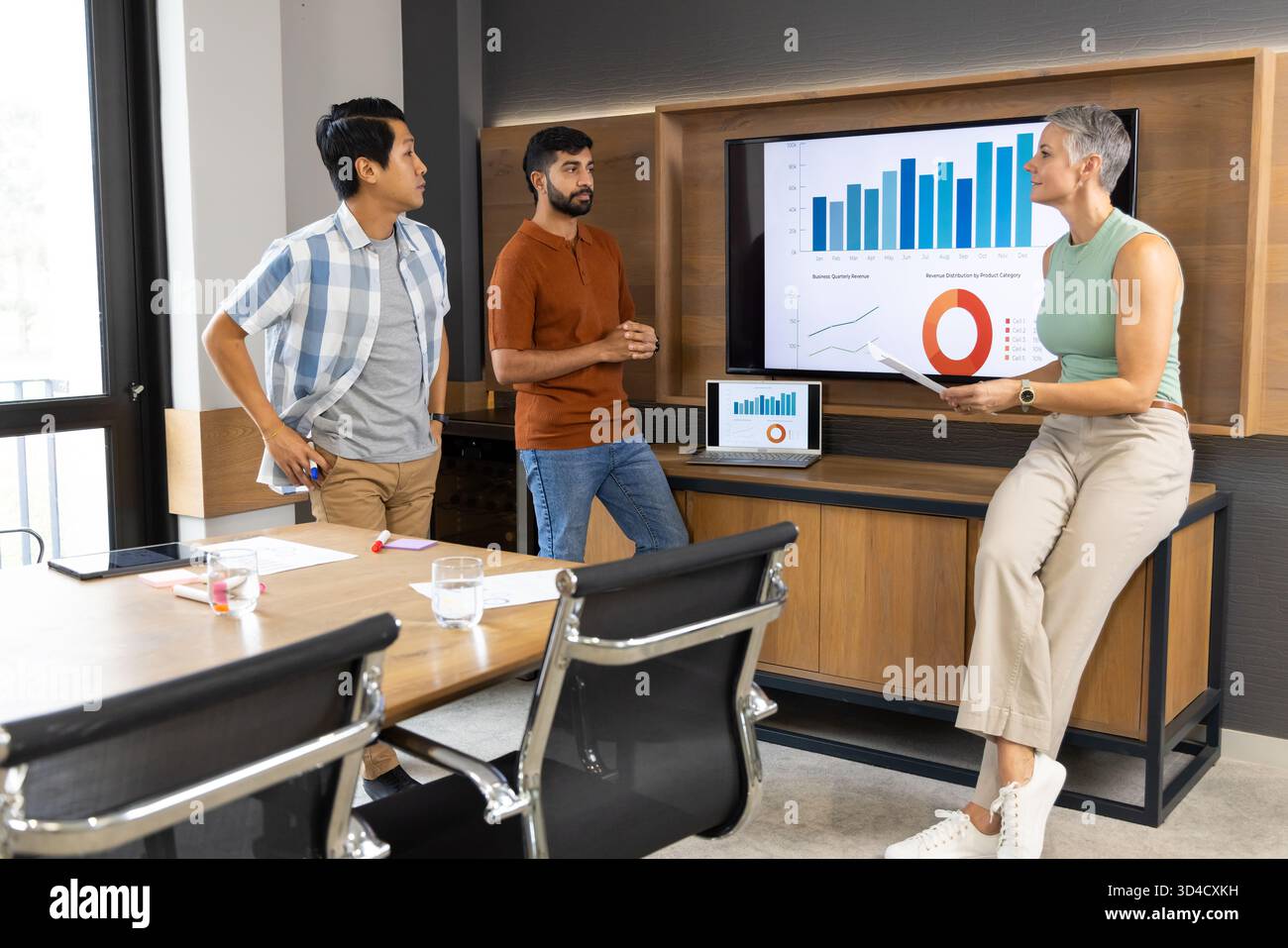 Divers collègues discutent de la présentation des données dans une salle de conférence moderne, avec moniteur et ordinateur portable Banque D'Images
