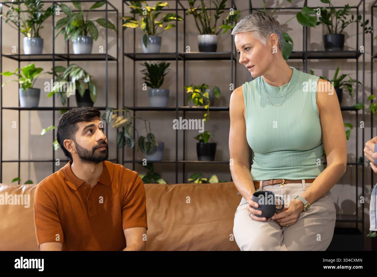 Divers collègues assis sur le canapé en cuir dans le salon de bureau, tenant une tasse à café et admirant les plantes Banque D'Images