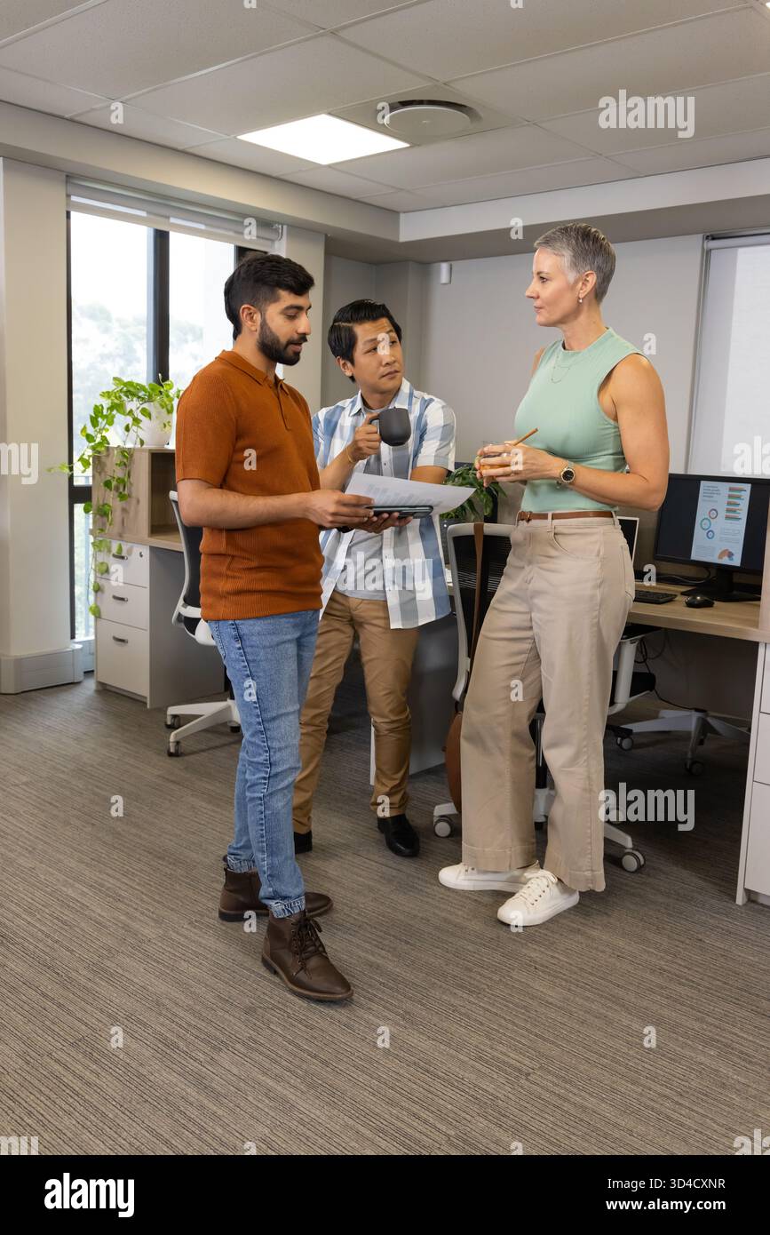 Divers collègues discutent des détails du projet dans un bureau ouvert, avec des documents imprimés et des tasses à café Banque D'Images