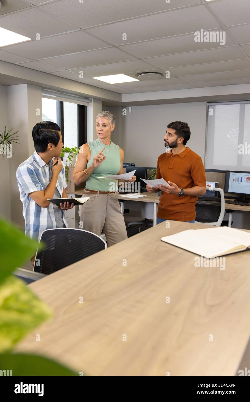 Divers collègues discutent autour du bureau dans un bureau ouvert, avec des tablettes papier et un ordinateur portable Banque D'Images