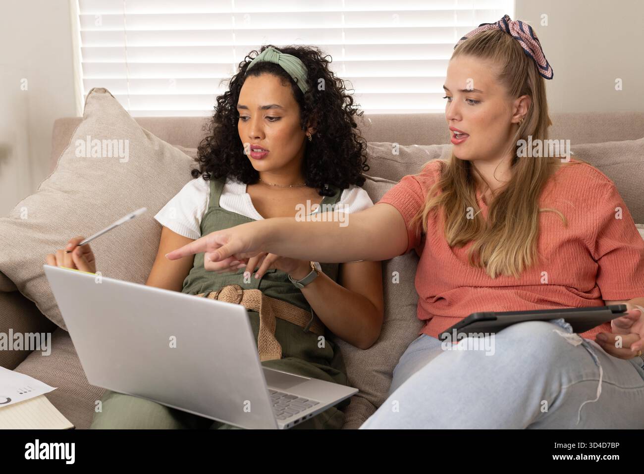 Examen des notes diverses amies féminines assises sur le canapé dans le salon, avec ordinateur portable, tablette, papiers Banque D'Images