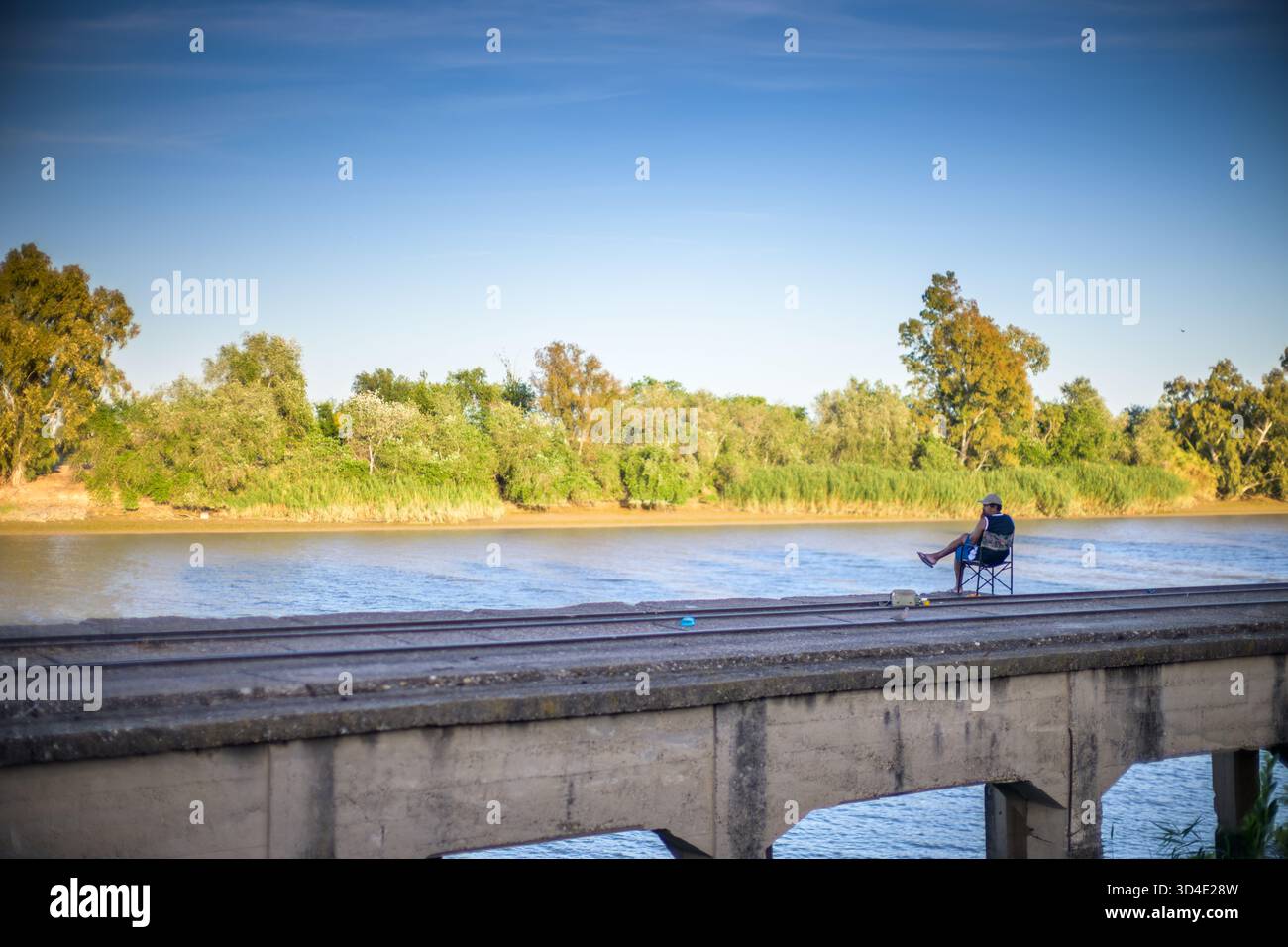 Un local se détend sur une chaise près du Guadalquivir, profitant de la solitude et de la brise du soir à l'ancien quai de train minier à San Juan de Aznalfarache. Banque D'Images