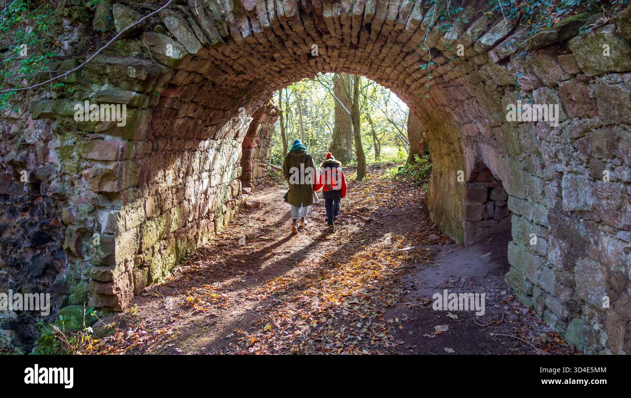 Vue d'une mère et d'un enfant marchant à travers un tunnel voûté en pierre, la lumière du soleil battant le chemin devant, Haddington, Écosse, Royaume-Uni. Banque D'Images