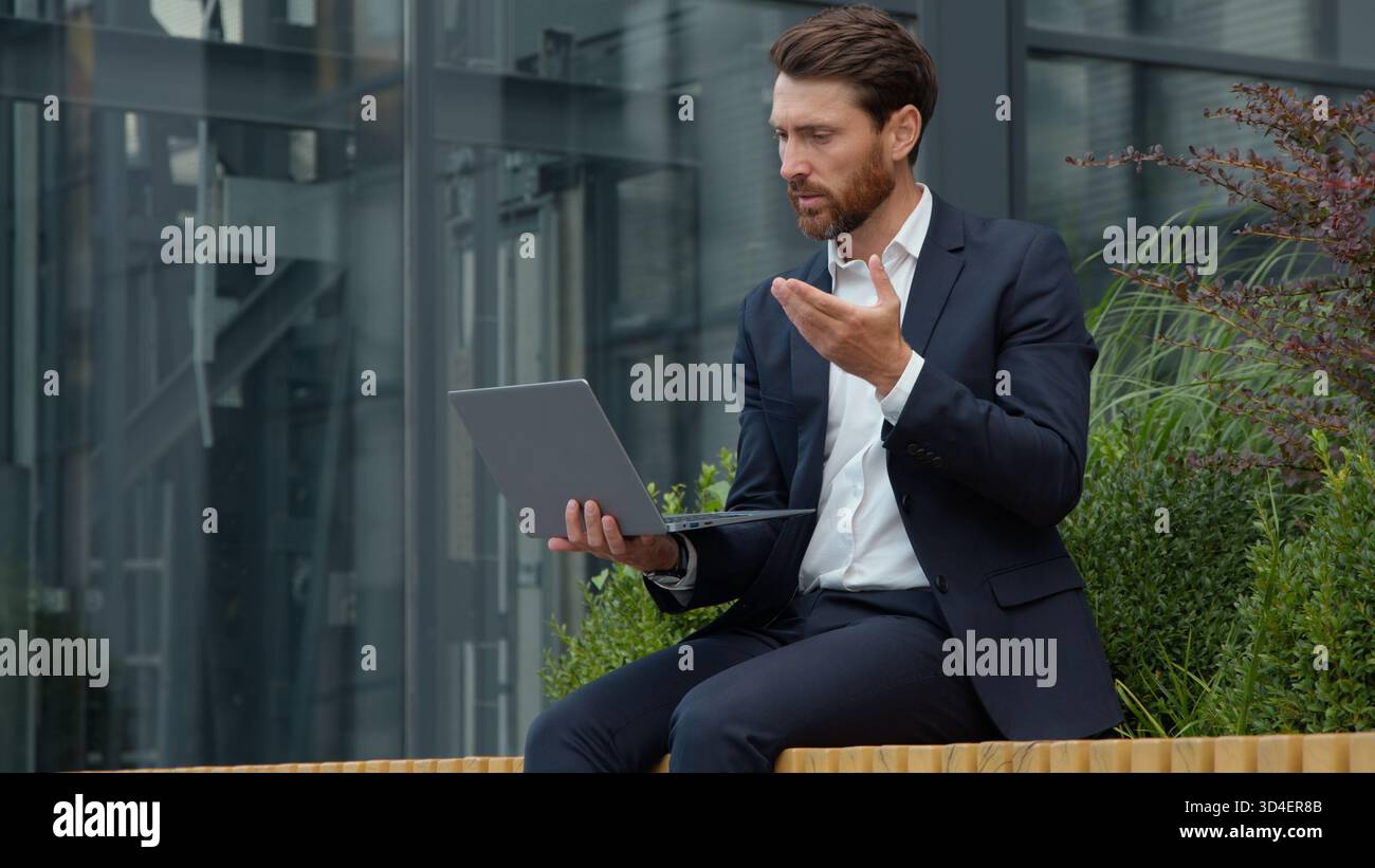Homme d'affaires mature caucasien professionnel parlant appel vidéo avec ordinateur portable dans la ville consultant homme d'affaires masculin assis à l'extérieur communiquant avec Banque D'Images