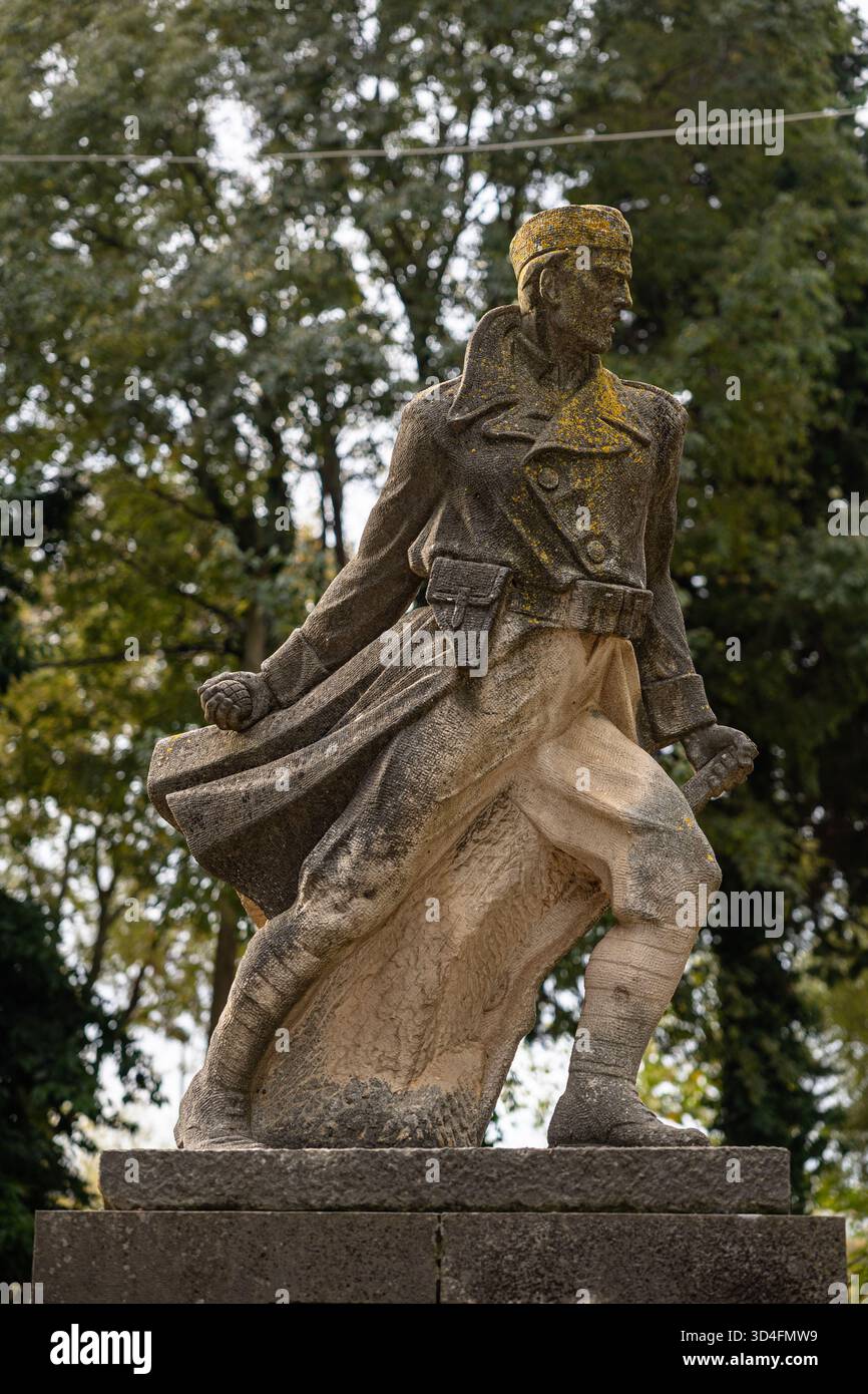 Grohote, CROATIE, 10.23.2025 :Statue en pierre extérieure d'un soldat en marche au sommet d'un piédestal de brique, flanqué de plaques nominatives. Des fleurs fraîches reposent à la base Banque D'Images