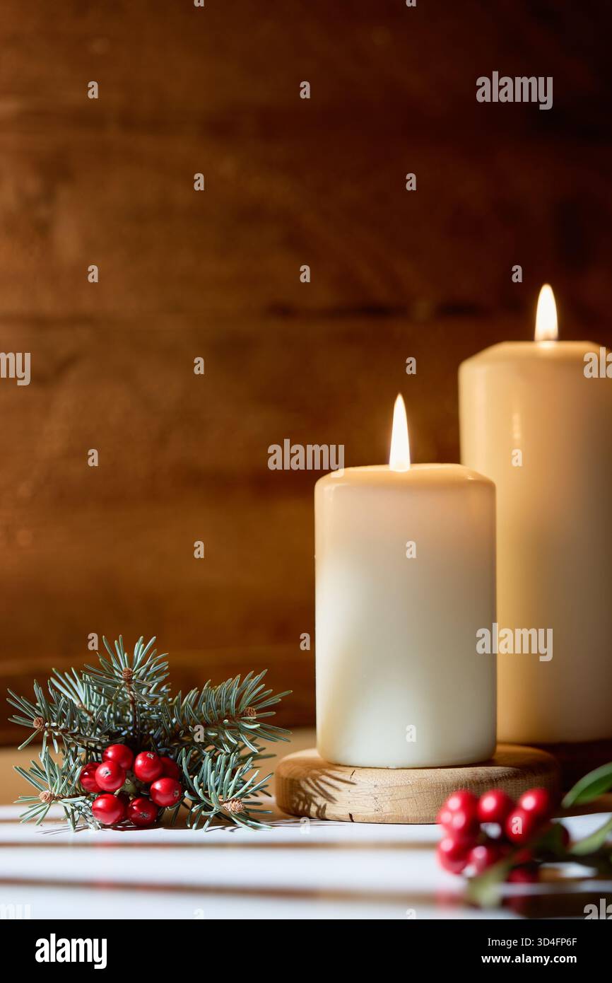 Cozy Christmas Still Life avec deux bougies blanches brûlantes, des branches de pin et des baies de houx rouges Banque D'Images
