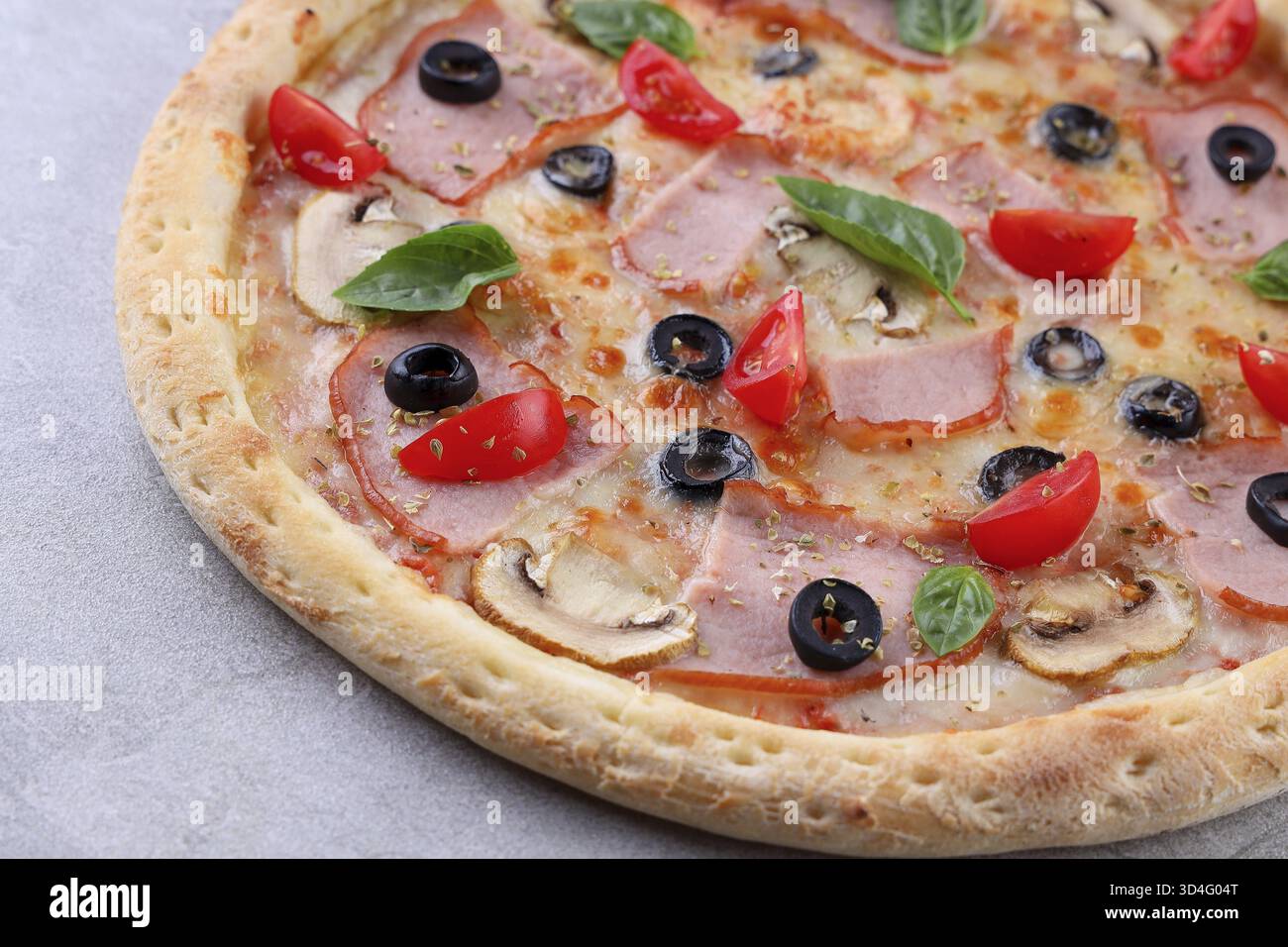 Nourriture, pizza cuite au feu de bois garnie de tranches de jambon fumé, d'olives noires, de champignons sautés, de tomates cerises coupées en deux et de feuilles de basilic frais sur un golde Banque D'Images