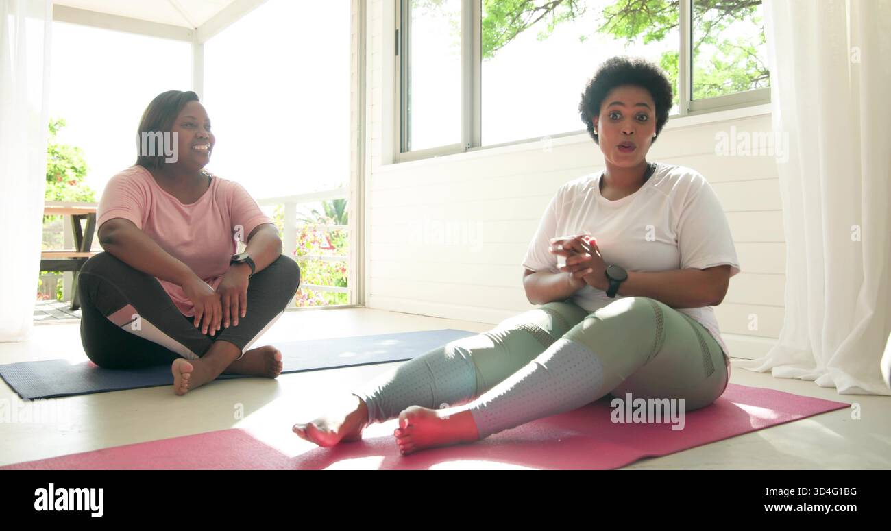 Femme gestuelle en leggings verts assis sur un tapis rose dans une véranda avec tapis bleu, montre-bracelet Banque D'Images