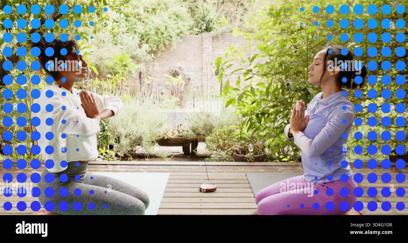 Agenouillement deux femmes portant des vêtements de sport pressant les paumes sur une terrasse en bois avec des tapis de yoga et un bol chantant Banque D'Images