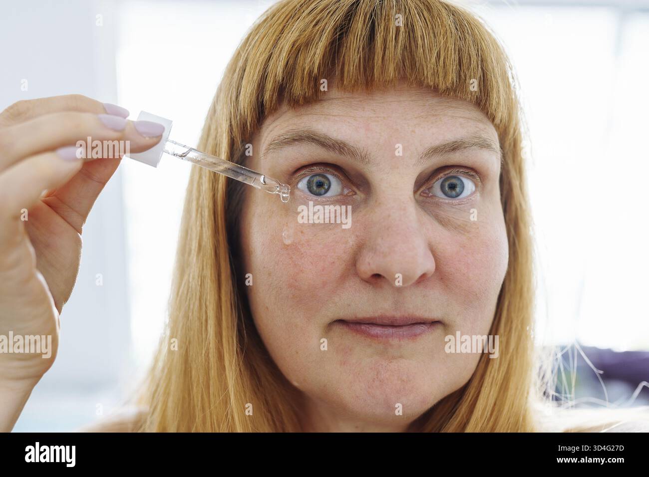 Visage femme d'âge moyen gros plan, blonde, application de produit cosmétique contre le vieillissement de la peau, visage, contre les rides sous les yeux Banque D'Images