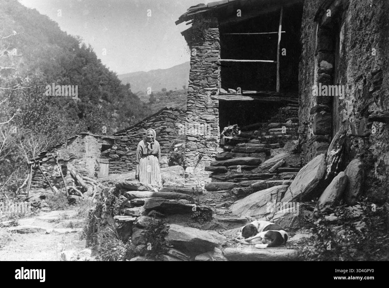 Vue partielle d'une maison avec un toit en ardoise à Montseny, avec une femme et un chien. Capturé par Josep Maria Armengol i Bas entre 1899 et 1905. Cette image reflète la vie rurale et l'architecture dans la région de Montseny en Catalogne. Banque D'Images