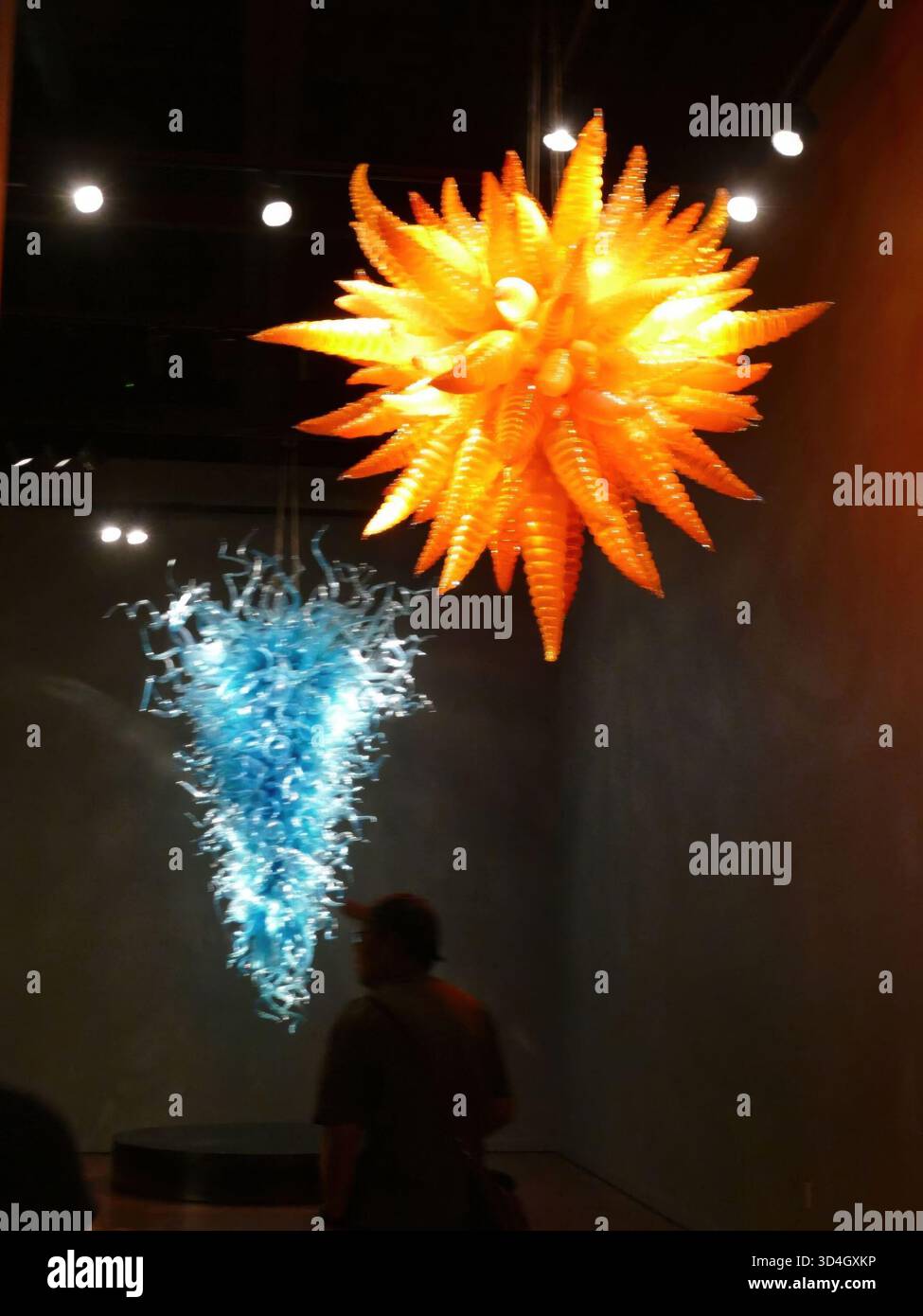 SEATTLE - APR 25, 2025 - deux lustres en verre coloré, un orange et un bleu, sont suspendus au plafond d'une pièce sombre, créant un intéressant Banque D'Images