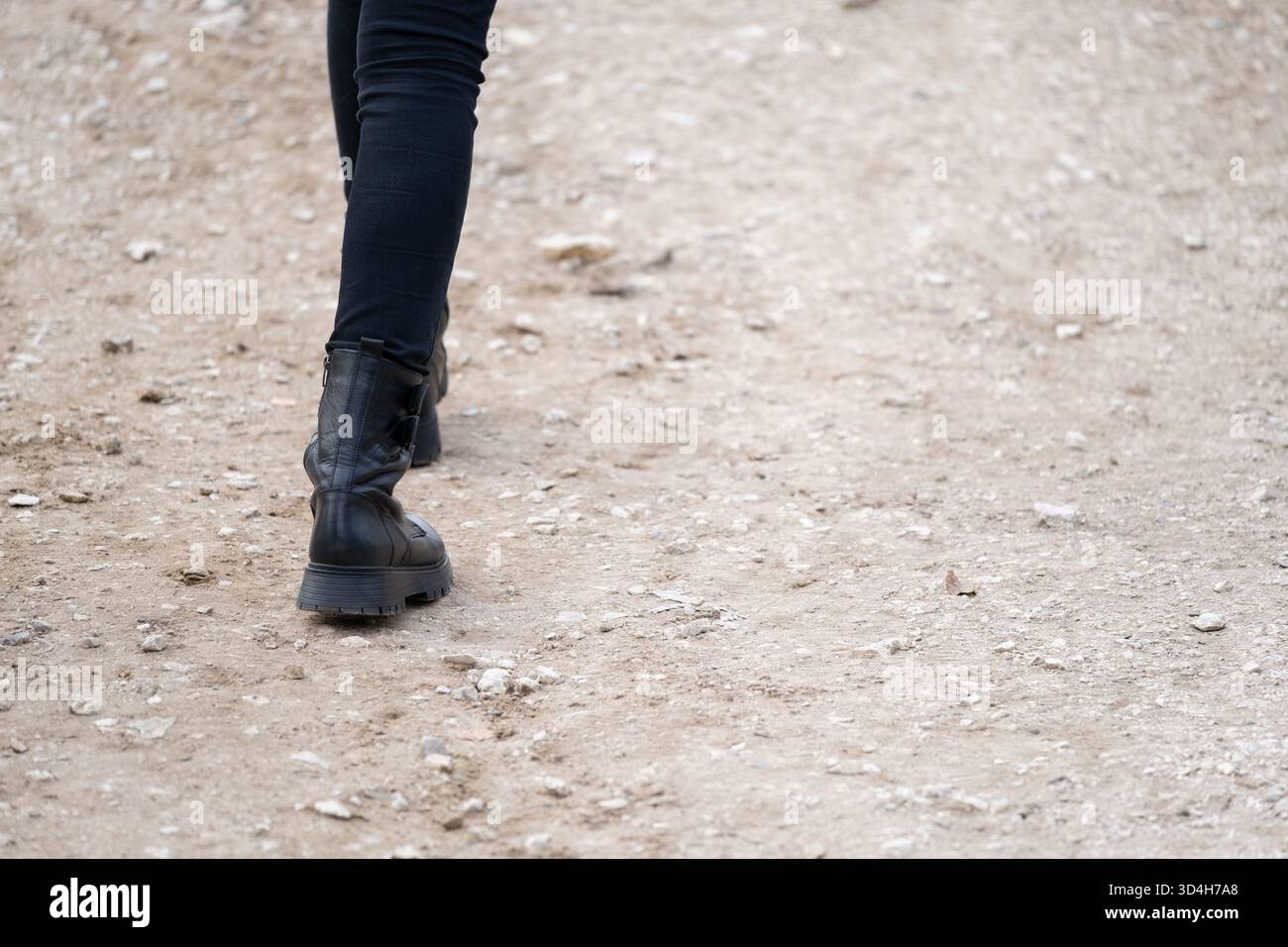 Vue rapprochée d'une personne marchant le long d'un sentier extérieur poussiéreux dans des bottes noires. Cette image convient aux projets sur la randonnée, la marche urbaine, les voyages, ou Banque D'Images